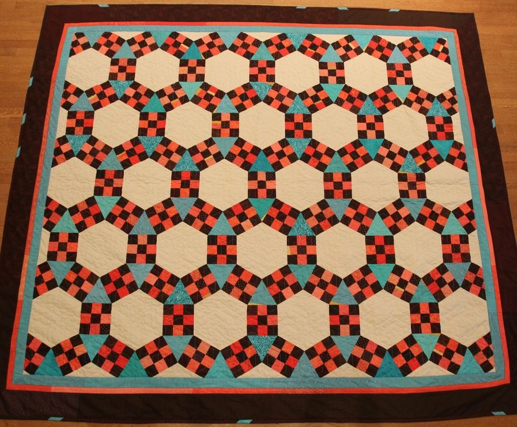an aerial view of a quilt with large cream-colored hexagons, medium-sized teal triangles, and small brown and coral-colored squares